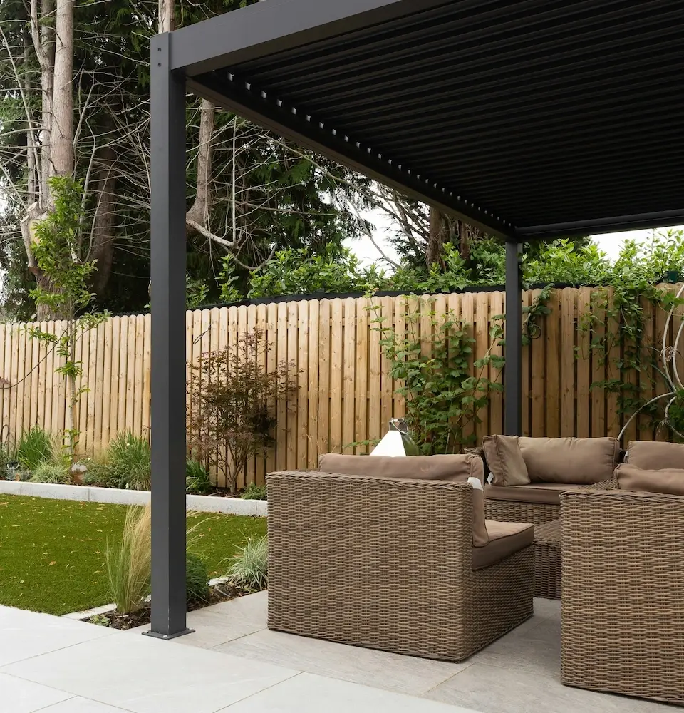 Black pergola with outdoor sofa on a paved patio and wooden privacy fence